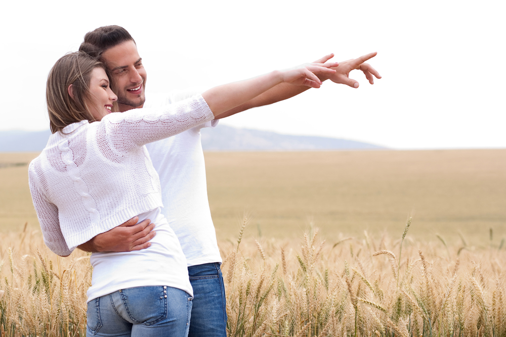 Young couple in meadow pointing in the air, hugging in the park